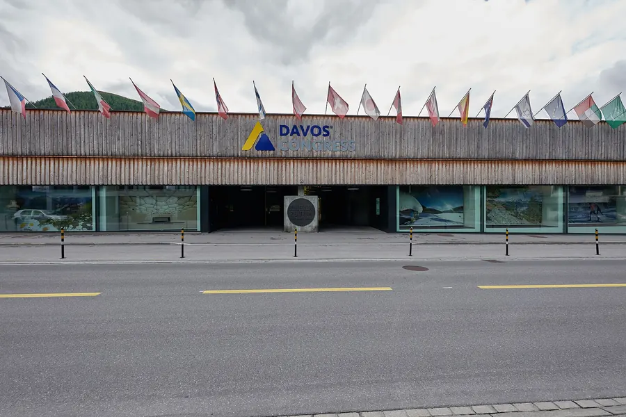 The Davos Congress Centre, a large modern building in a snowless alpine valley with mountains behind.