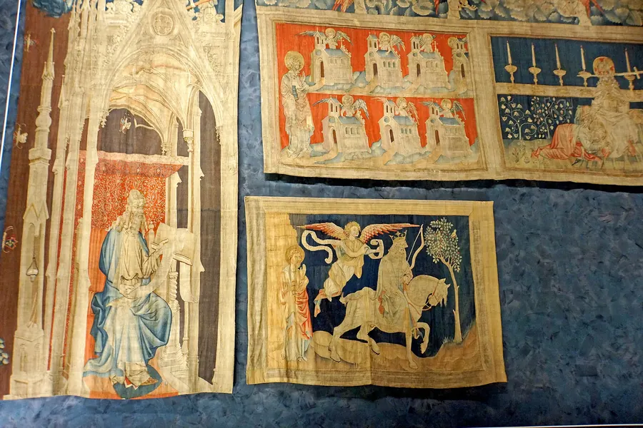 Sections of a medieval tapestry on display, with figures from scenes of the Book of Revelation.