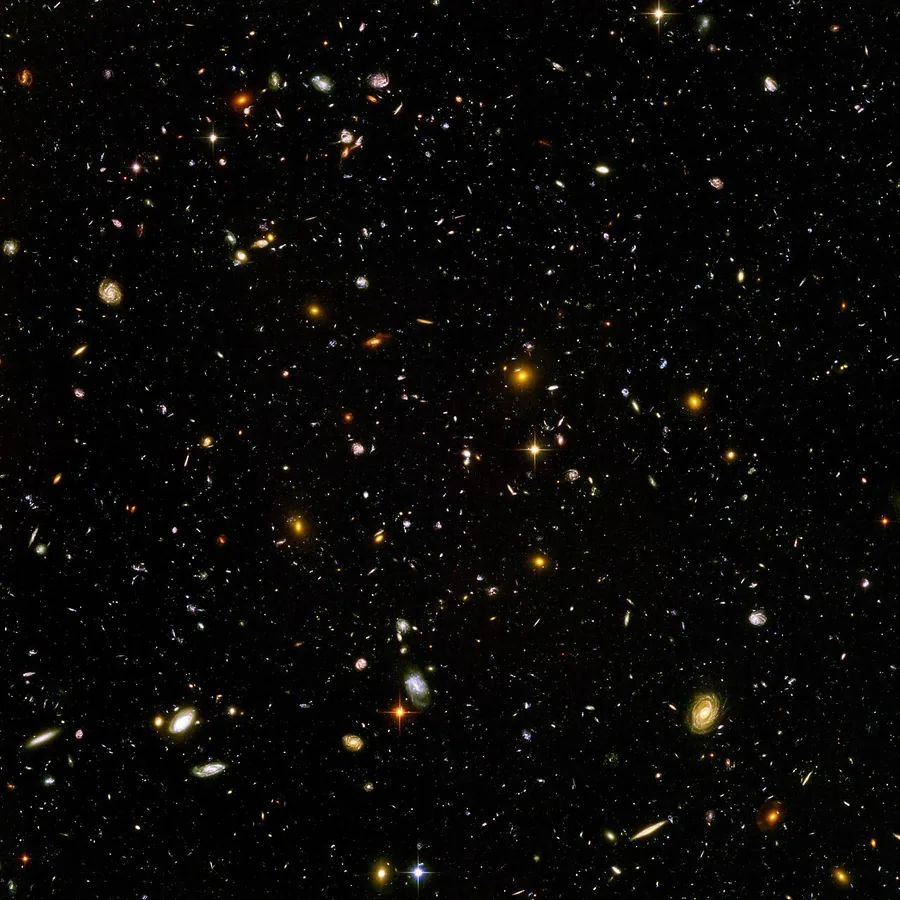 A dark field scattered with thousands of small galaxies of many shapes and colors.