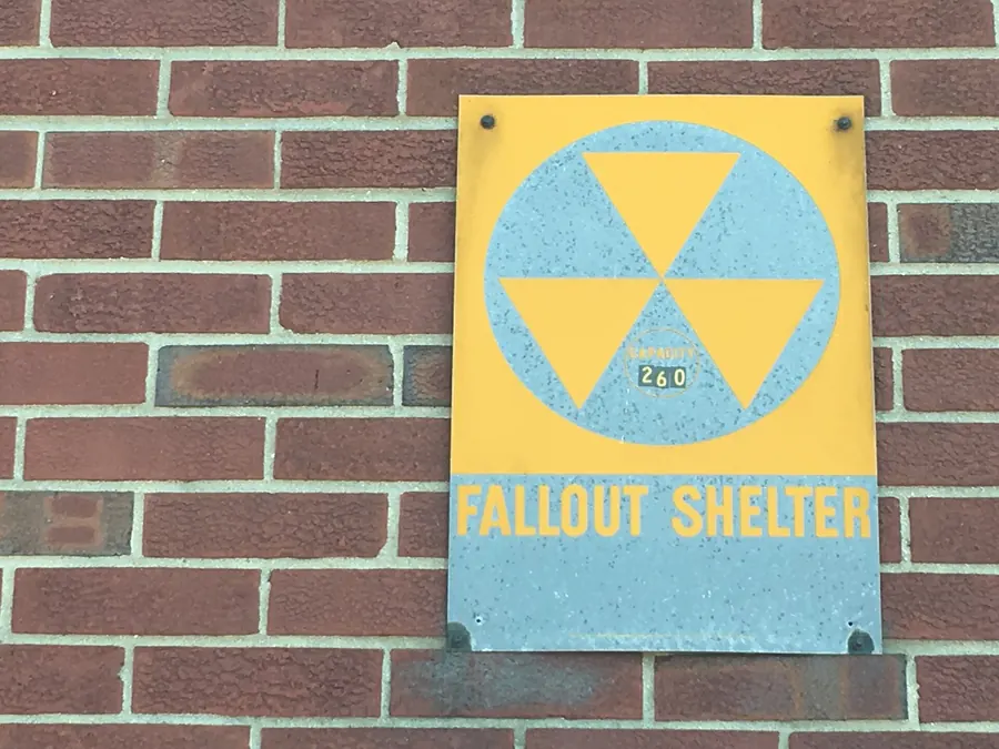 A yellow and black fallout shelter sign on a brick building.
